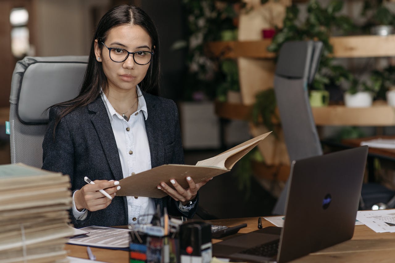 Confident businesswoman in professional attire reviewing documents at her desk in a modern office setting.